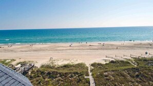 A beach with a clear view of the ocean, sandy shore, and a pathway leading to a building.