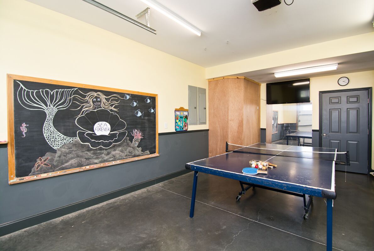 Une pièce avec une table de ping-pong, une grande fresque murale et un coin cuisine à l’arrière-plan.