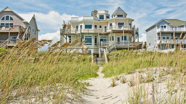 A beachfront property with multiple levels, a central staircase, and a sandy pathway leading to the entrance.