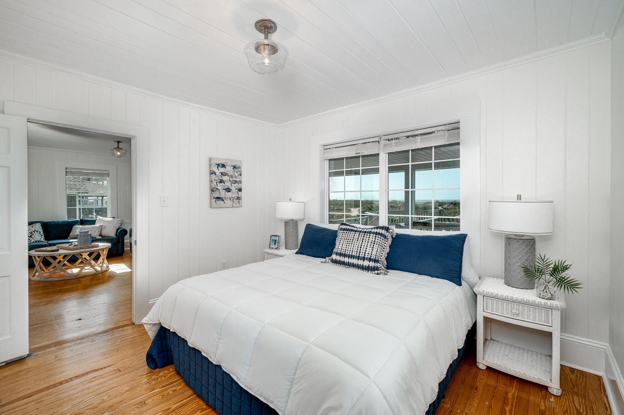 A bedroom with a large bed, two bedside tables with lamps, a window with blinds, and a view of the outdoors.