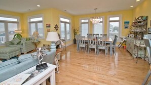 A spacious living room with a dining area, yellow walls, and a chandelier. - Sea Notes, Almost Oceanfront House in Emerald Isle, NC! (Emerald Isle)