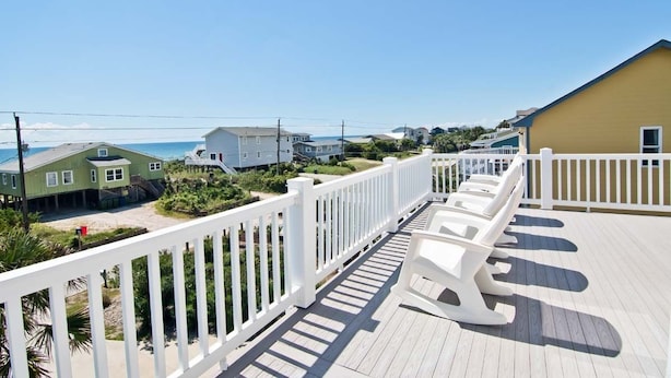 A wooden deck with white railings and lounge chairs overlooking a beach with houses in the background. - Sea Notes, Almost Oceanfront House in Emerald Isle, NC! (Emerald Isle)