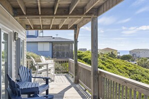 A wooden deck with Adirondack chairs and a table, overlooking a lush green landscape and houses. - Summervilla, Almost Oceanfront House in Emerald Isle, NC! (Emerald Isle)