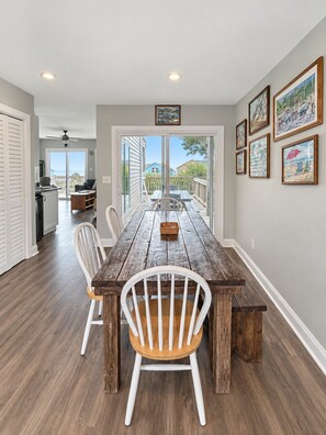 A dining area with a wooden table and chairs, a view to the outside, and artwork on the walls.