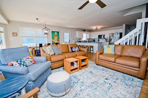 A spacious living room with a sofa set, ottoman, and a dining area with a high table.