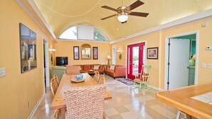 A spacious living area with a high ceiling, a wooden dining table, and a red door. - Sunbeam, Oceanside House in Emerald Isle, NC! (Emerald Isle)
