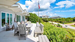 Une terrasse extérieure couverte, dotée de fauteuils Adirondack et d’une table, qui offre une vue sur un paysage verdoyant et luxuriant ainsi que sur une route.