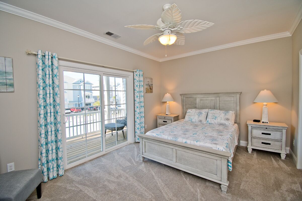 A bedroom with a bed, two bedside tables, a ceiling fan, and a view of the outside through a sliding glass door.