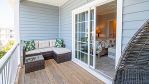A covered porch with a wicker sofa and a wicker chair, a sliding glass door leading to a bedroom, and a view of the outside balcony. - Seaside Villas 44, Soundside Townhouse in Atlantic Beach, NC! (Atlantic Beach)