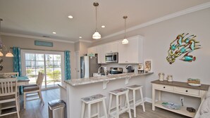 A modern kitchen with white cabinets, a central island with stools, a microwave, and a sink. - Seaside Villas 44, Soundside Townhouse in Atlantic Beach, NC! (Atlantic Beach)