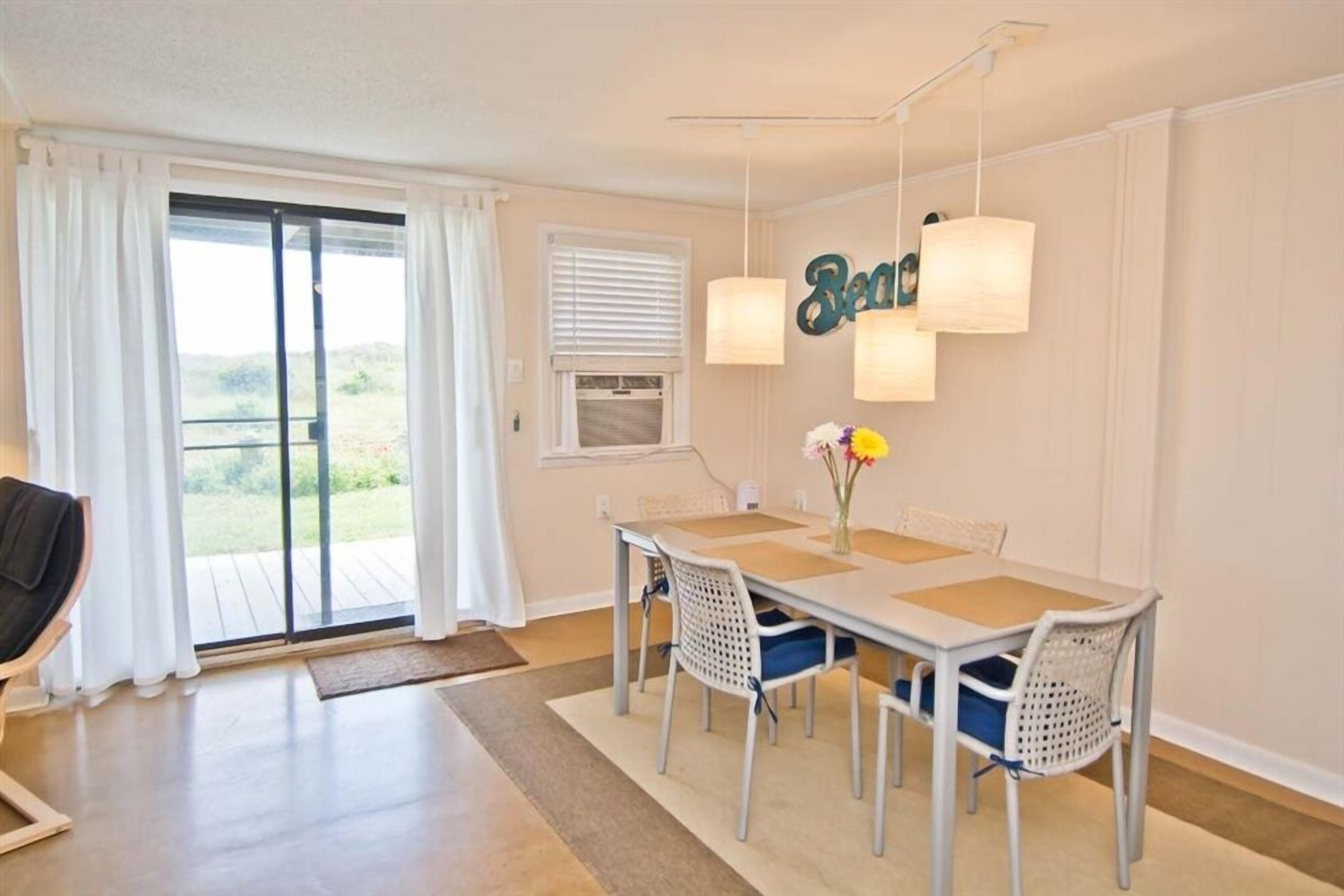 Un coin repas avec une table et des chaises, une vue à travers une porte-fenêtre coulissante et un luminaire fixé au mur.
