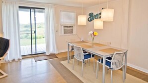 A dining area with a table and chairs, a view through a sliding glass door, and a wall-mounted light fixture. - Sunny Daze, Almost Oceanfront Duplex in Atlantic Beach, NC! (Atlantic Beach)