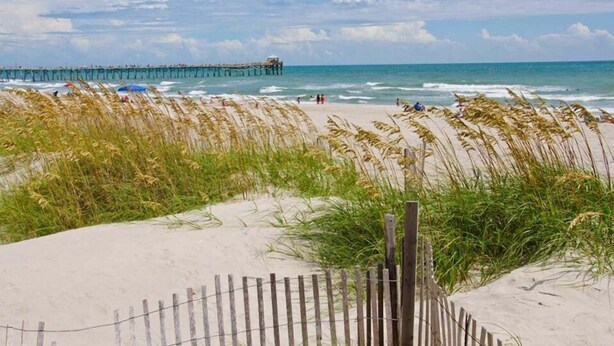 A beach with sand dunes, a wooden fence, and a pier in the background. - Sunny Daze, Almost Oceanfront Duplex in Atlantic Beach, NC! (Atlantic Beach)