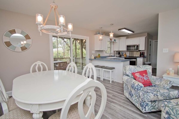 A modern kitchen with white cabinets, a central island, and a dining area with a white table and chairs. - Sunny Side, Soundside House in Emerald Isle, NC! (Emerald Isle)