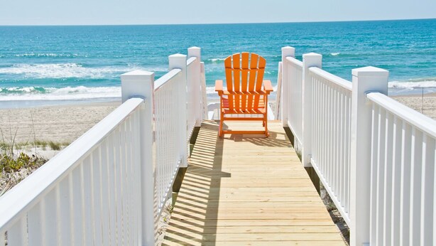 Une promenade en bois menant à une plage où se trouve une seule chaise orange.