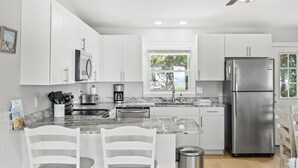 Una cocina moderna con armarios blancos, un refrigerador de acero inoxidable y una encimera de mármol.