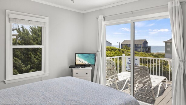 Un dormitorio con cama, televisión y balcón con sillas y vista al océano.