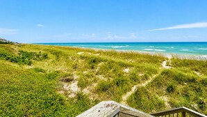 Un paysage côtier avec un ciel dégagé, des dunes herbeuses et une plage de sable.