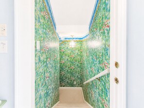 Un couloir avec un papier peint à motifs et une porte blanche dotée d’une poignée en laiton.