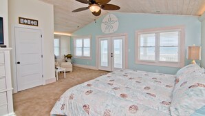 A bedroom with a large bed, a ceiling fan, a desk with a chair, and a door with a fish decoration. - Swiss House, Oceanfront Home in Atlantic Beach, NC! (Atlantic Beach)