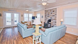 A cozy living room with two light blue sofas, a wooden floor, a stone wall, and a fireplace. - Swiss House, Oceanfront Home in Atlantic Beach, NC! (Atlantic Beach)