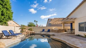 En swimmingpool med solstolar, ett område med grillplats och en uteplats med en pergola.