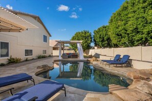 Un patio trasero con piscina, sillas de descanso y una pérgola.