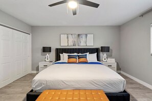 A bedroom with a bed, two bedside tables, a ceiling fan, a wall-mounted artwork, and a door. - Epic 6BR w/ Foosball + Popcorn | Pool + Fire Pit (Peoria)