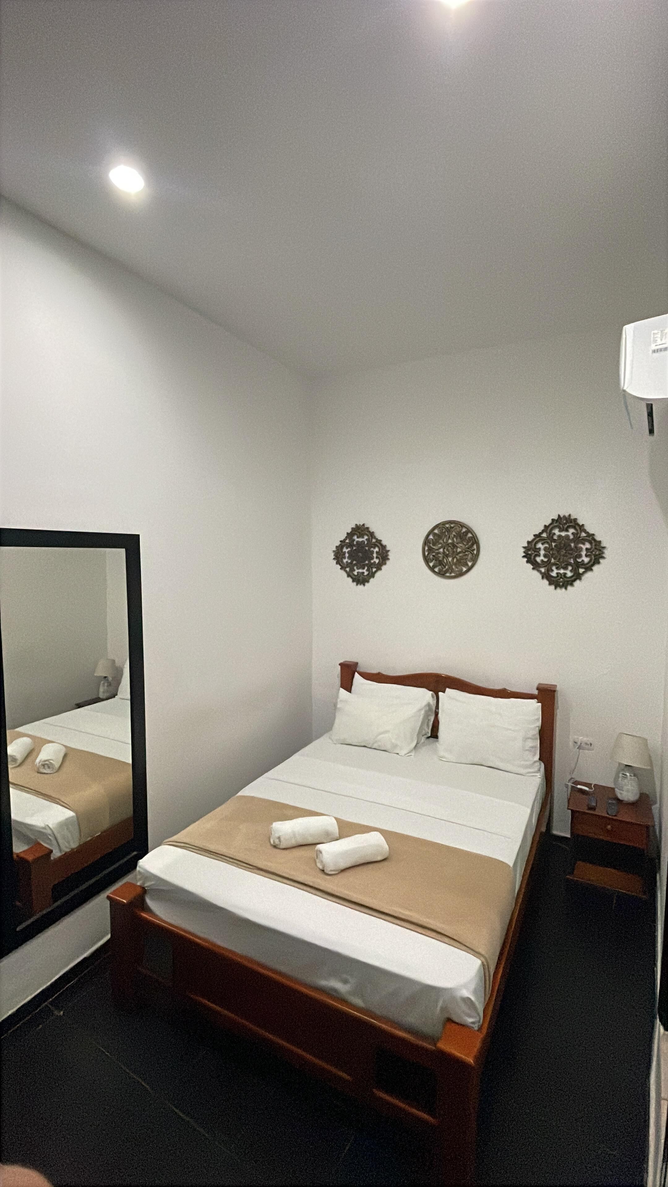 Une chambre d’hôtel avec un lit en bois, du linge de lit blanc, un miroir et des éléments décoratifs sur les murs.