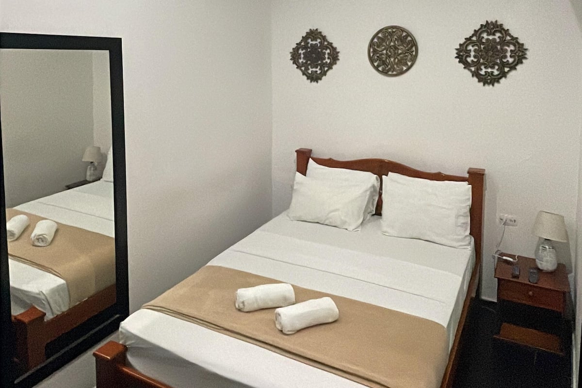 Una habitación de hotel con una cama de madera, ropa de cama blanca, un espejo y elementos decorativos en la pared.