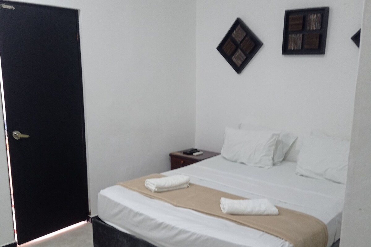 Une chambre d’hôtel avec un lit, une table de chevet, une porte et un cadre photo fixé au mur.
