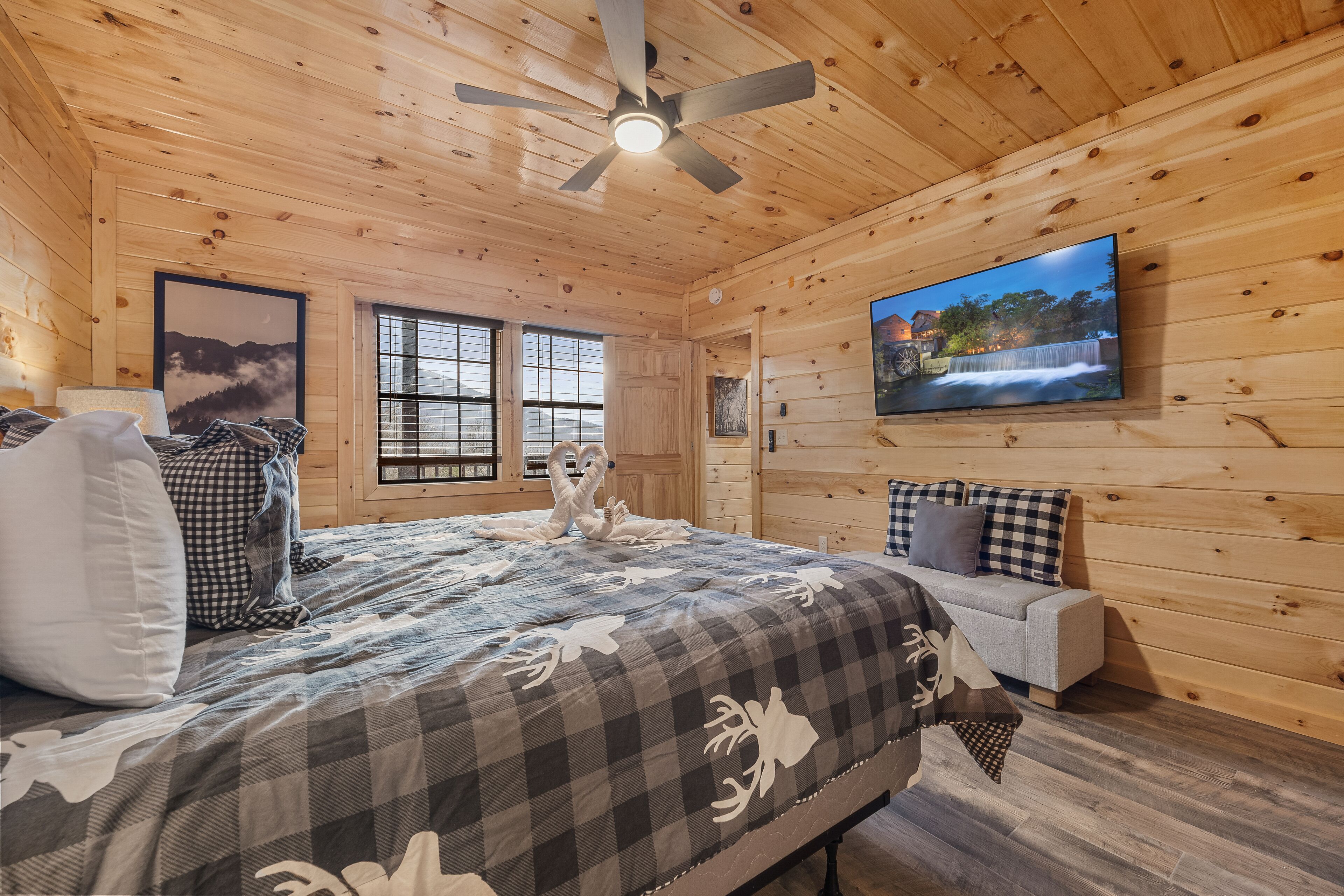 Une chambre de style cabane en bois, avec un lit, un canapé, un ventilateur de plafond, une télévision et des tableaux encadrés accrochés aux murs.