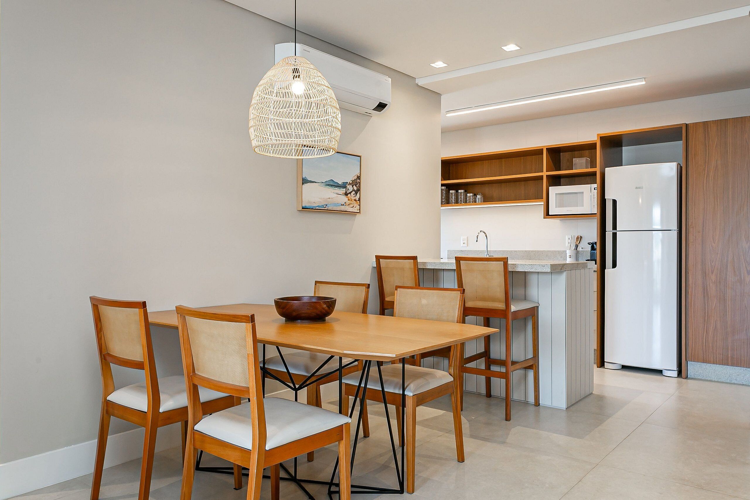 Een moderne keuken met een eethoek, met een houten tafel en stoelen, een hanglamp en inbouwplanken met keukenapparatuur.