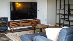 Ett vardagsrum med en stor tv-apparat med platt skärm, en möbel i trä för underhållningsutrustning, en soffa, ett litet runt bord och en svart hyllsektion.