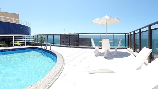 A rooftop pool area with lounge chairs and an umbrella, overlooking a cityscape and the sea. - Atlantic Ocean by SOLEMAR (Fortaleza)