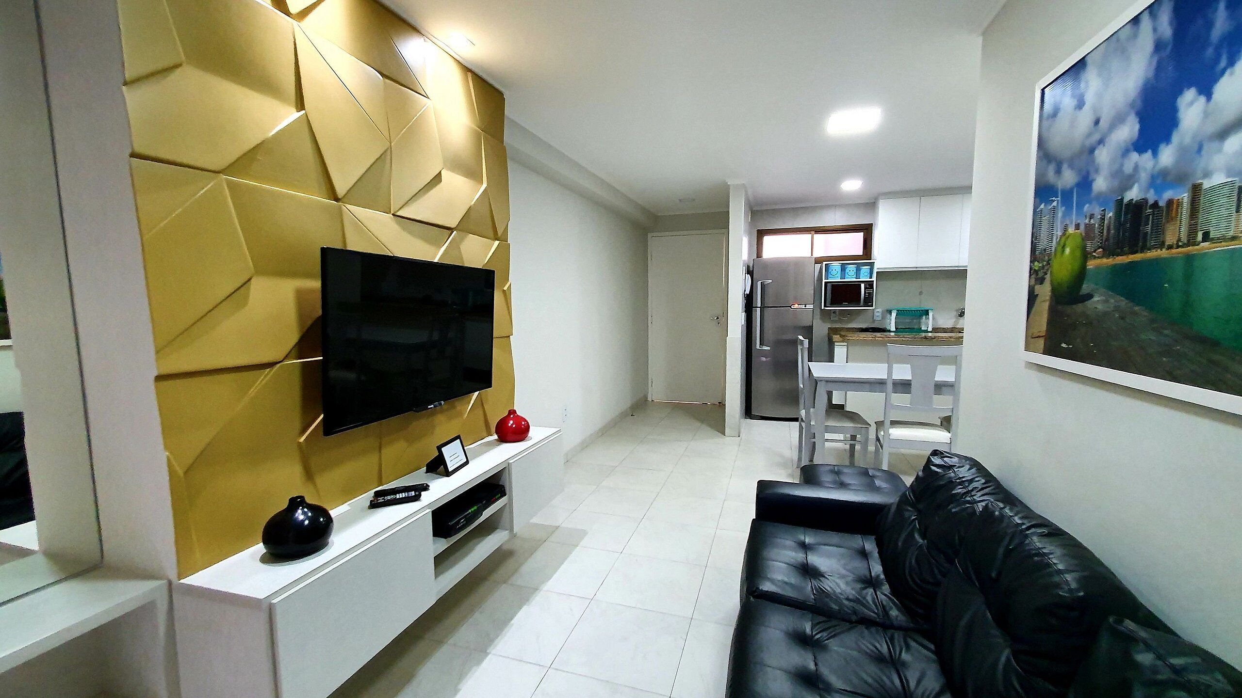 A modern living room with a flat-screen TV, a sofa, and a kitchen area in the background.