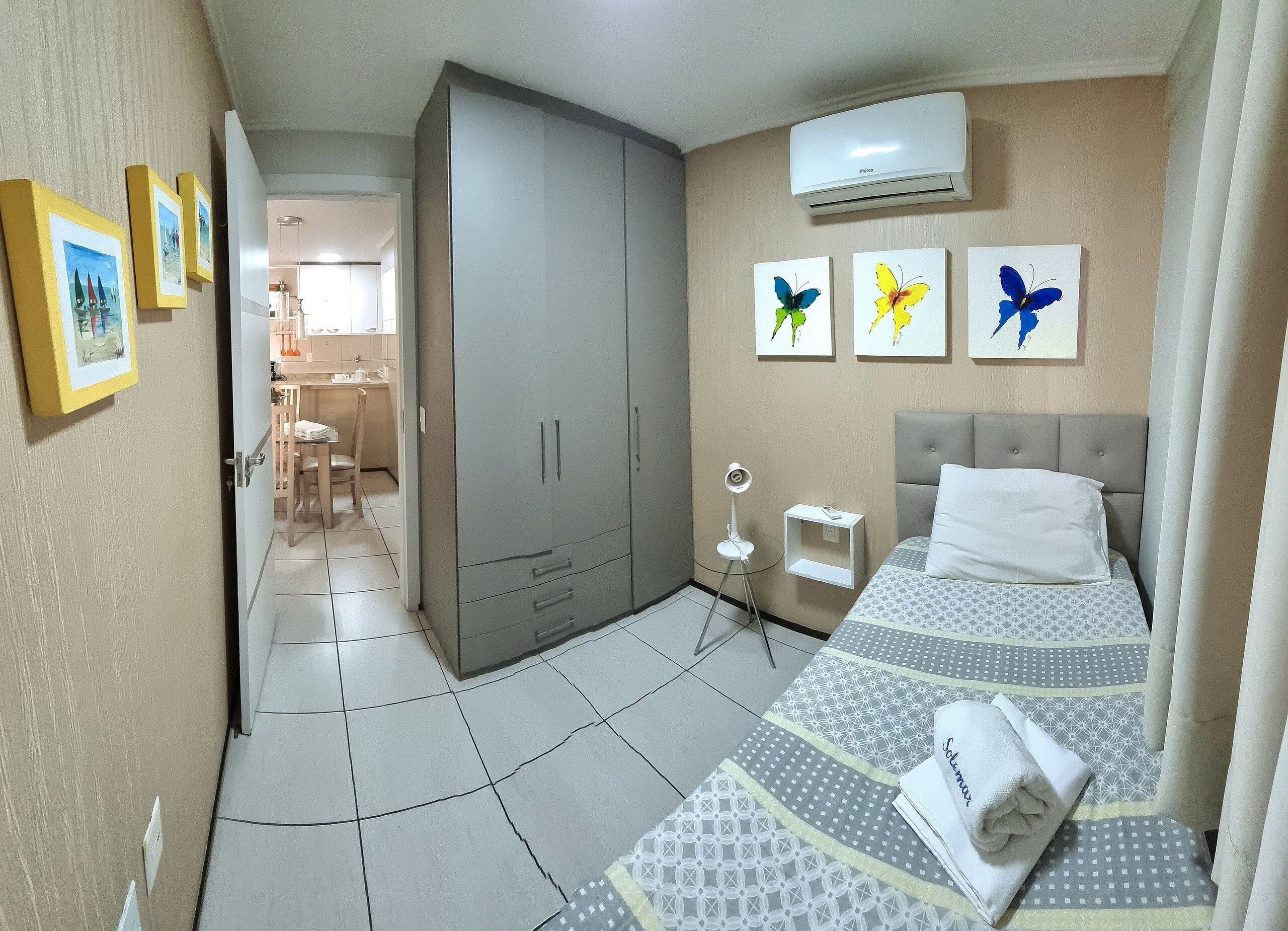 Ein Hotelzimmer mit Bett, Kleiderschrank, Schreibtisch und Stuhl. An der Wand befinden sich Schmetterlingsbilder.