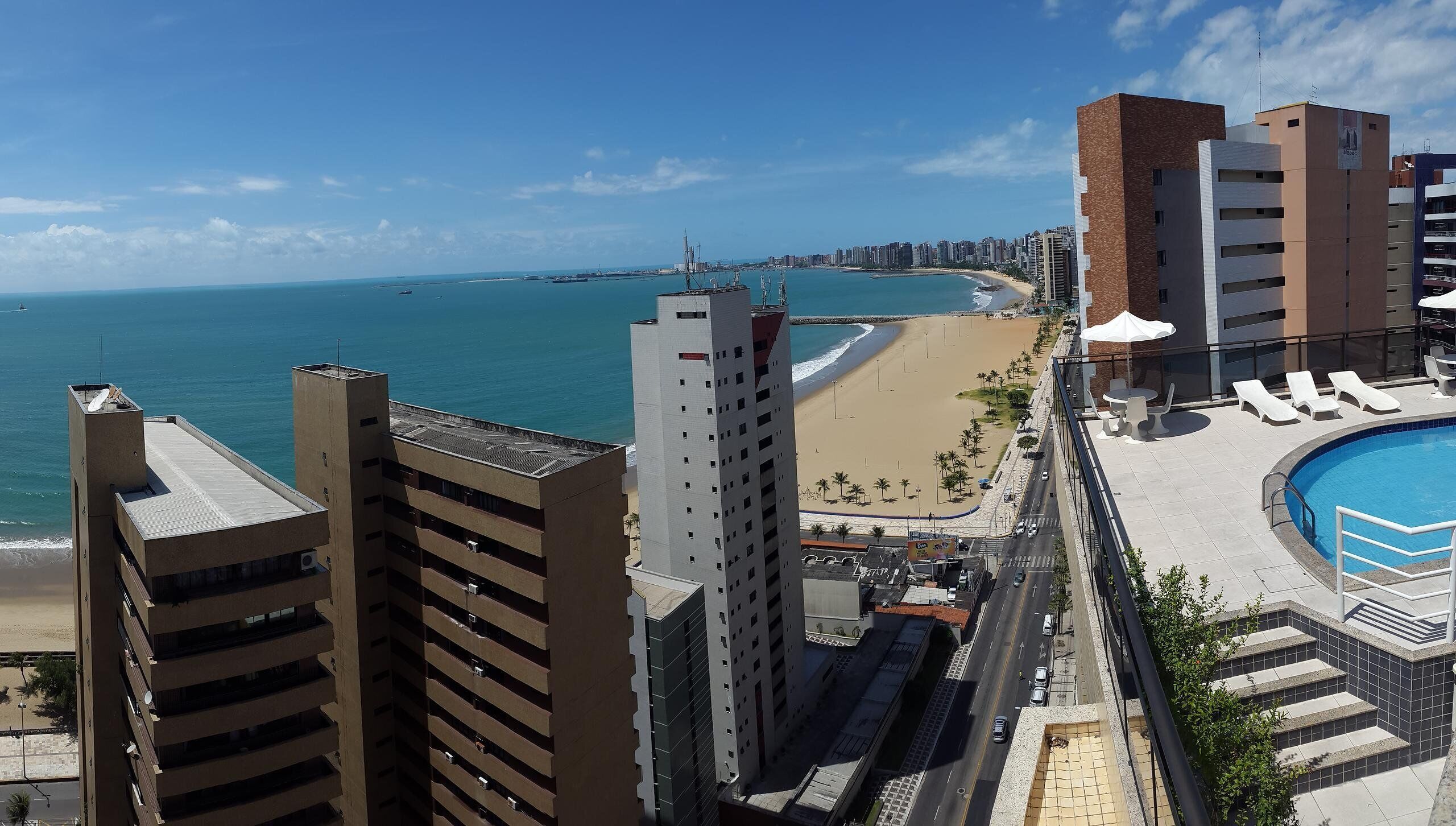 Un hotel de gran altura con piscina, vistas a la playa y un camino que lleva a ella.