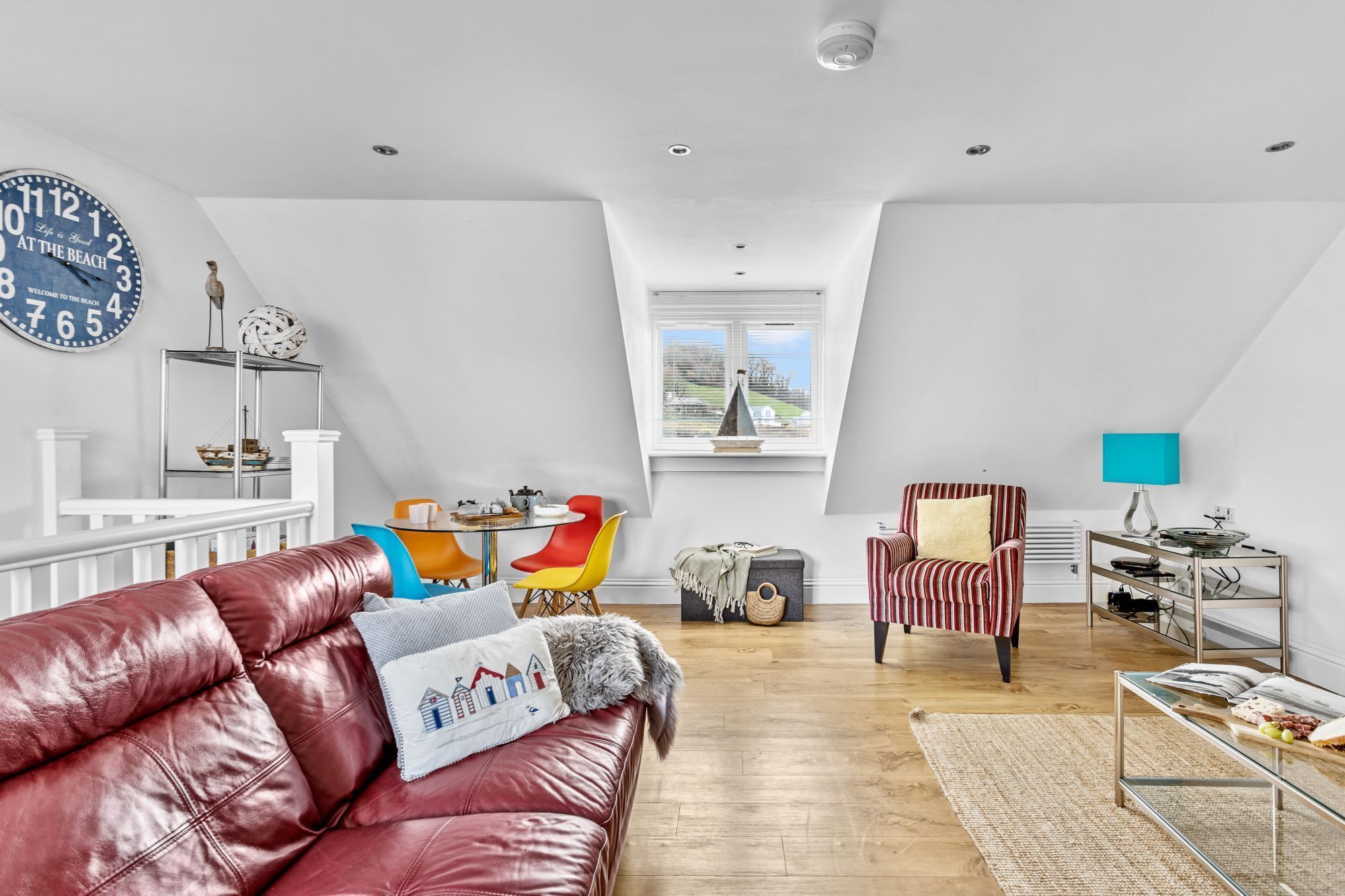Un loft spacieux avec un plafond haut, un coin repas avec des chaises colorées, un canapé en cuir et une vue à travers une lucarne.