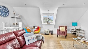 Een ruime loft met een hoge nok, een eethoek met kleurrijke stoelen, een leren bank en een uitzicht door een dakraam.