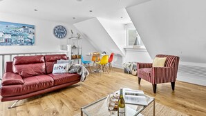 Een ruime loft met een hoge plafond, een eethoek met kleurrijke stoelen, een rode leren bank en een gestreept fauteuil.