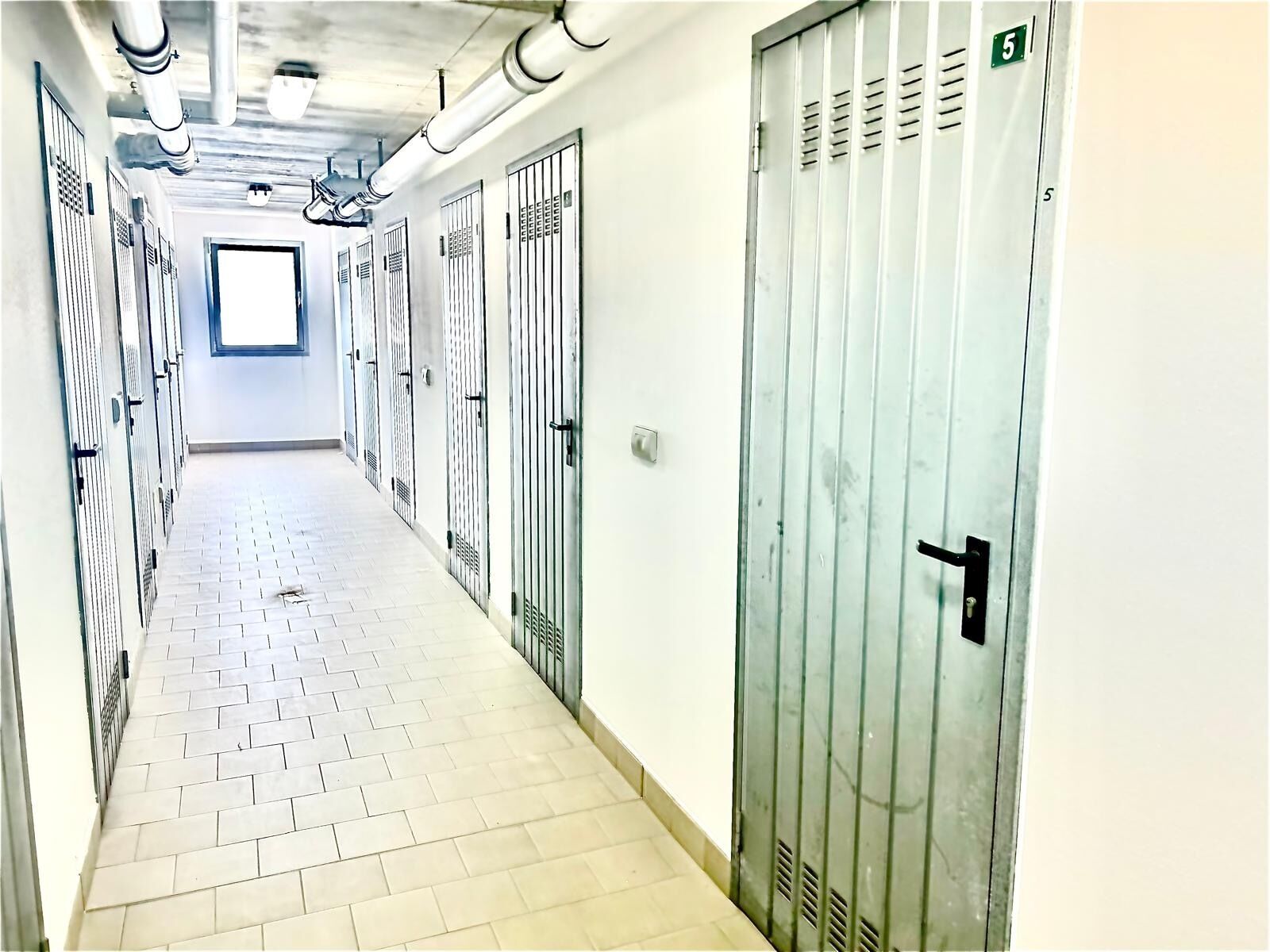 Ein Korridor mit Schließfächern, Fliesenboden und einem Fenster am Ende.