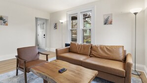 A living room with a brown leather sofa, a wooden coffee table, and a floor lamp. - Modern 4 BR/2 Bath House near University of Rochester (Rochester)