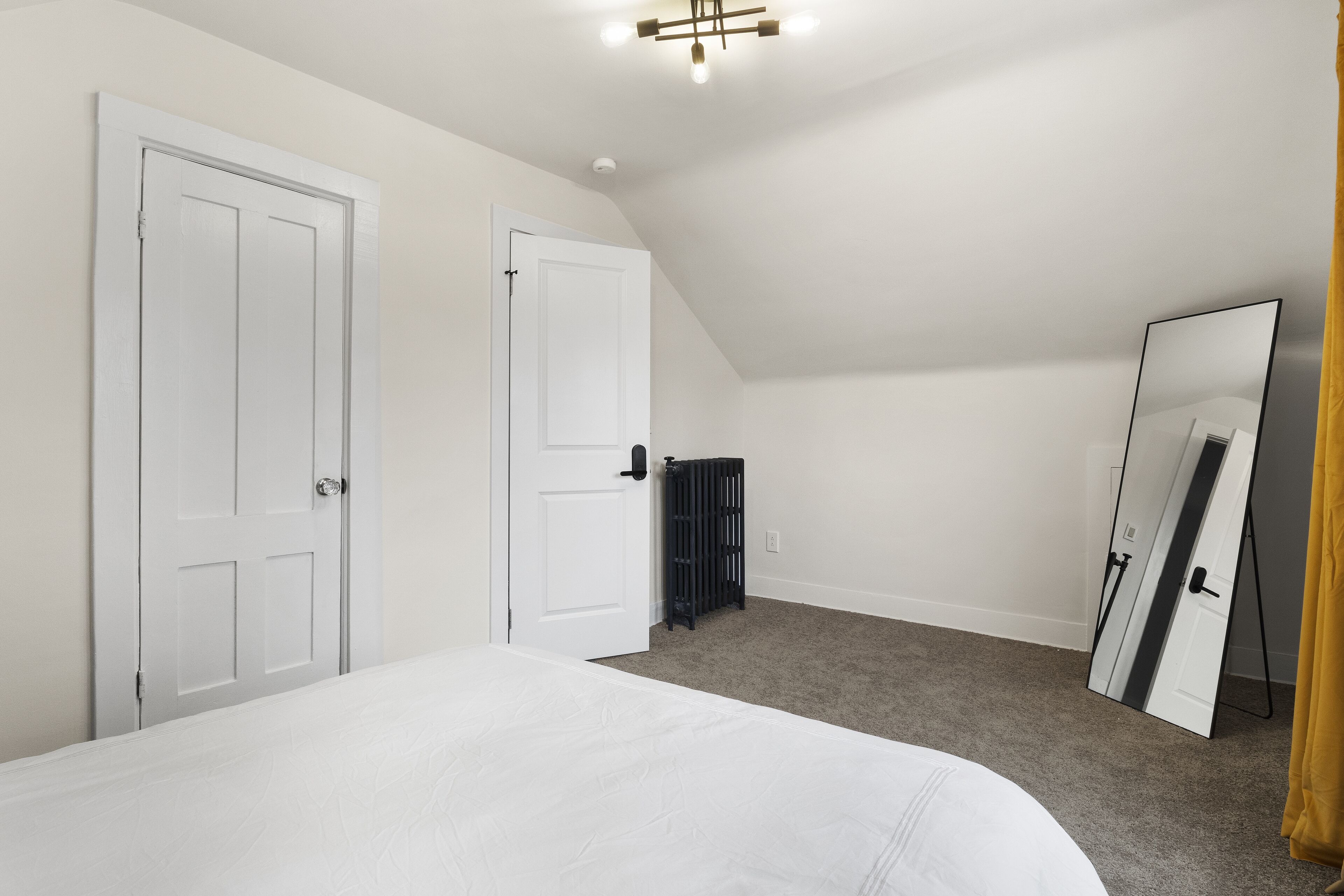 Une chambre avec un grand lit, deux portes blanches, un radiateur et un grand miroir.