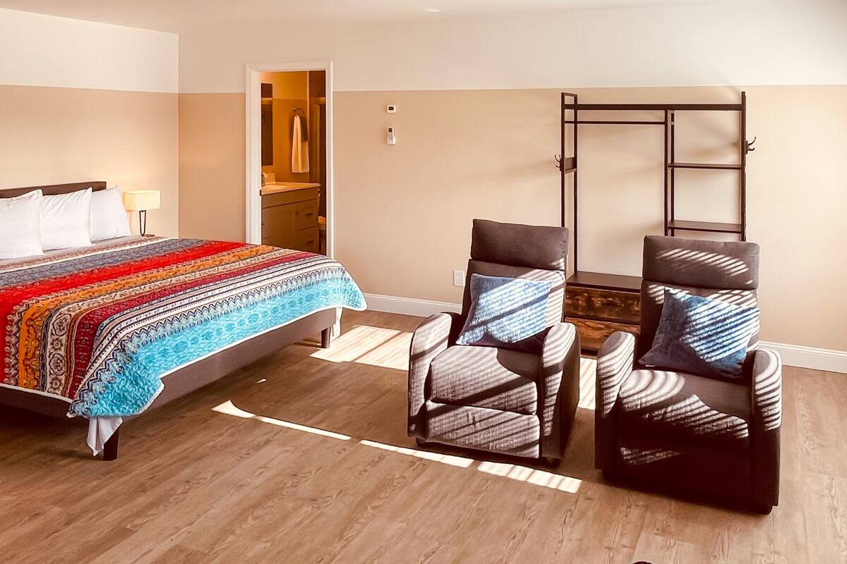 A bedroom with a bed, two armchairs, a small table, a ladder, and a bathroom door.