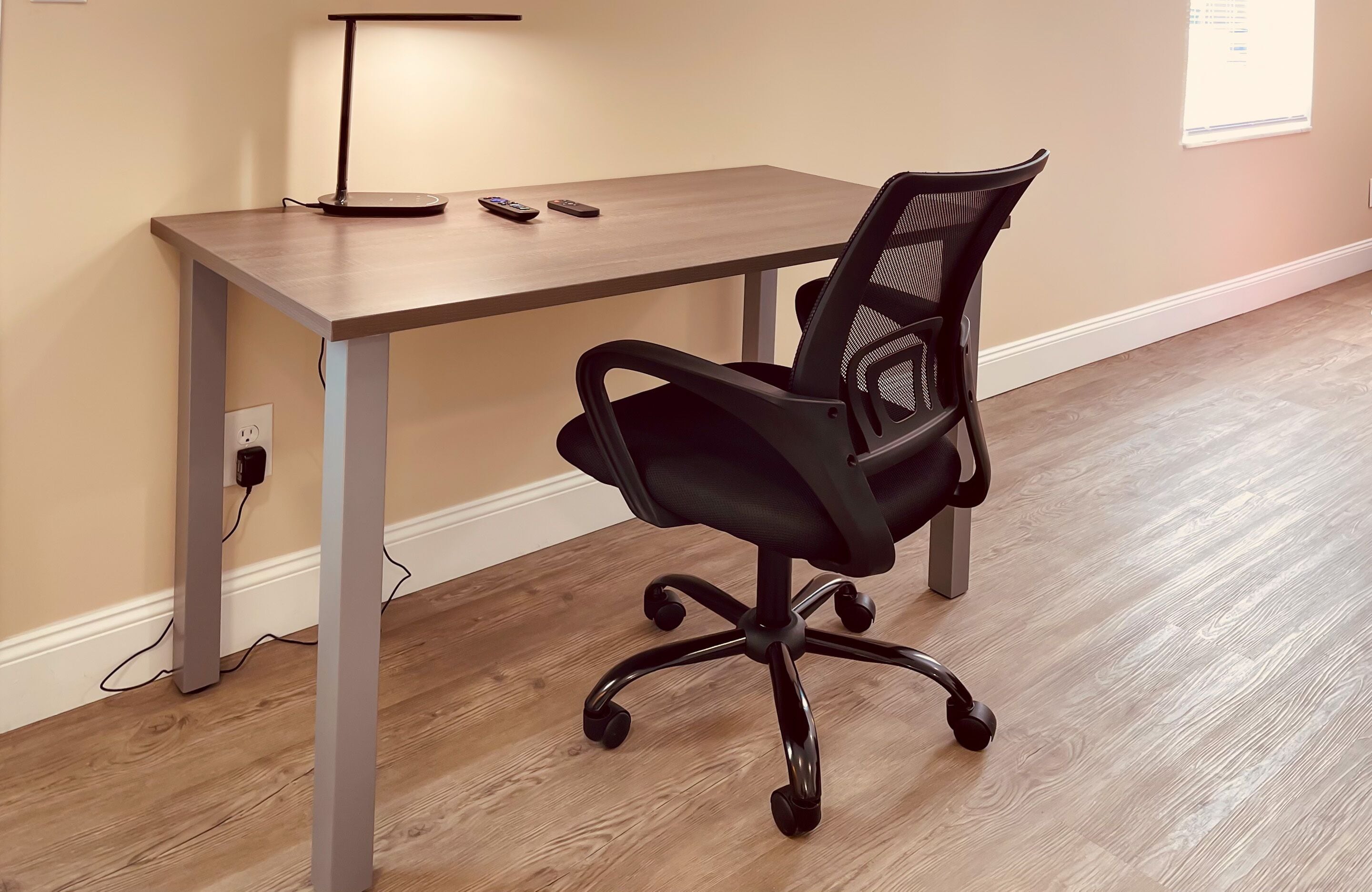 A modern office space with a wooden desk, a black office chair, and a lamp.