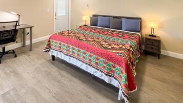 A bedroom with a bed, two bedside tables with lamps, a desk with a chair, and a door.