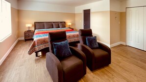 A bedroom with a bed, two armchairs, a nightstand, and a lamp.