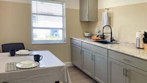 A compact kitchen with a dining area, featuring a window, a sink with a dish rack, and a countertop with kitchen utensils.