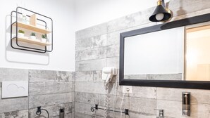 Een moderne badkamer met toilet, bidet en wastafel op een zuil, afgewerkt met grijze tegels en een houten accentmuur.